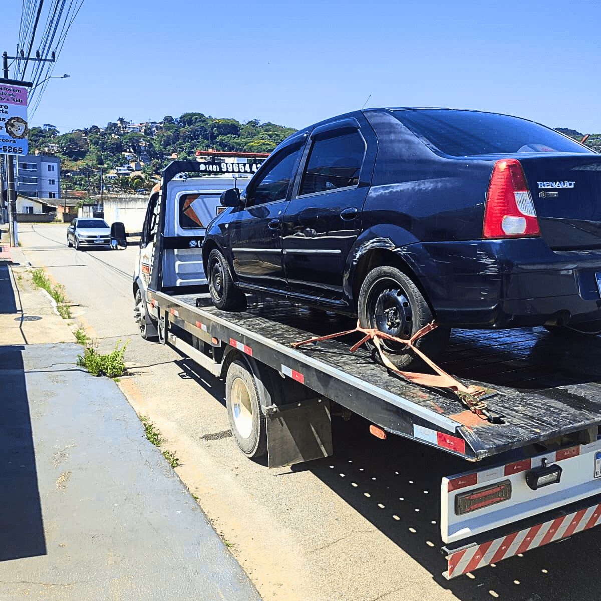 Serviço de reboque transportando carro sedan preto em área urbana de Palhoça com segurança.